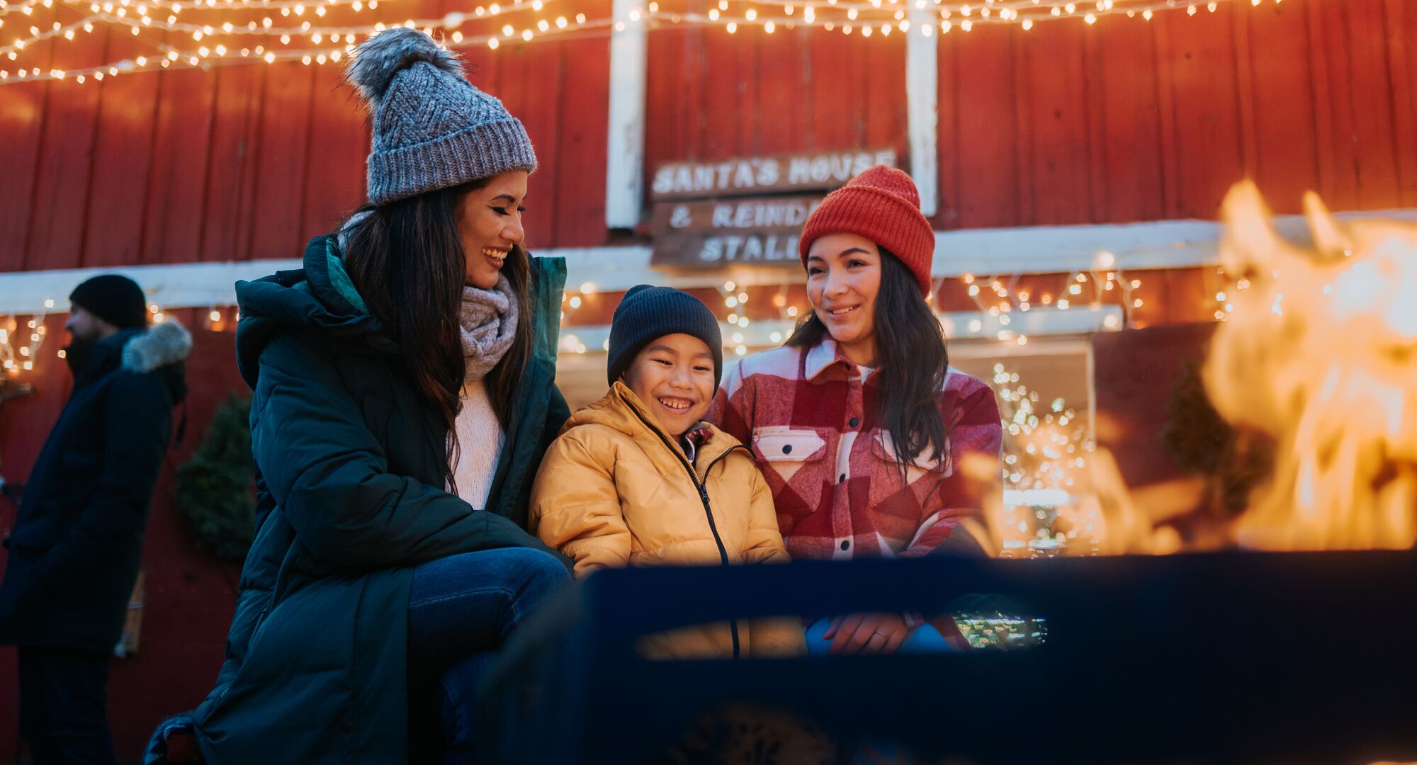 A family sitting around a fire at the Banff Christmas market with festive lights in the background